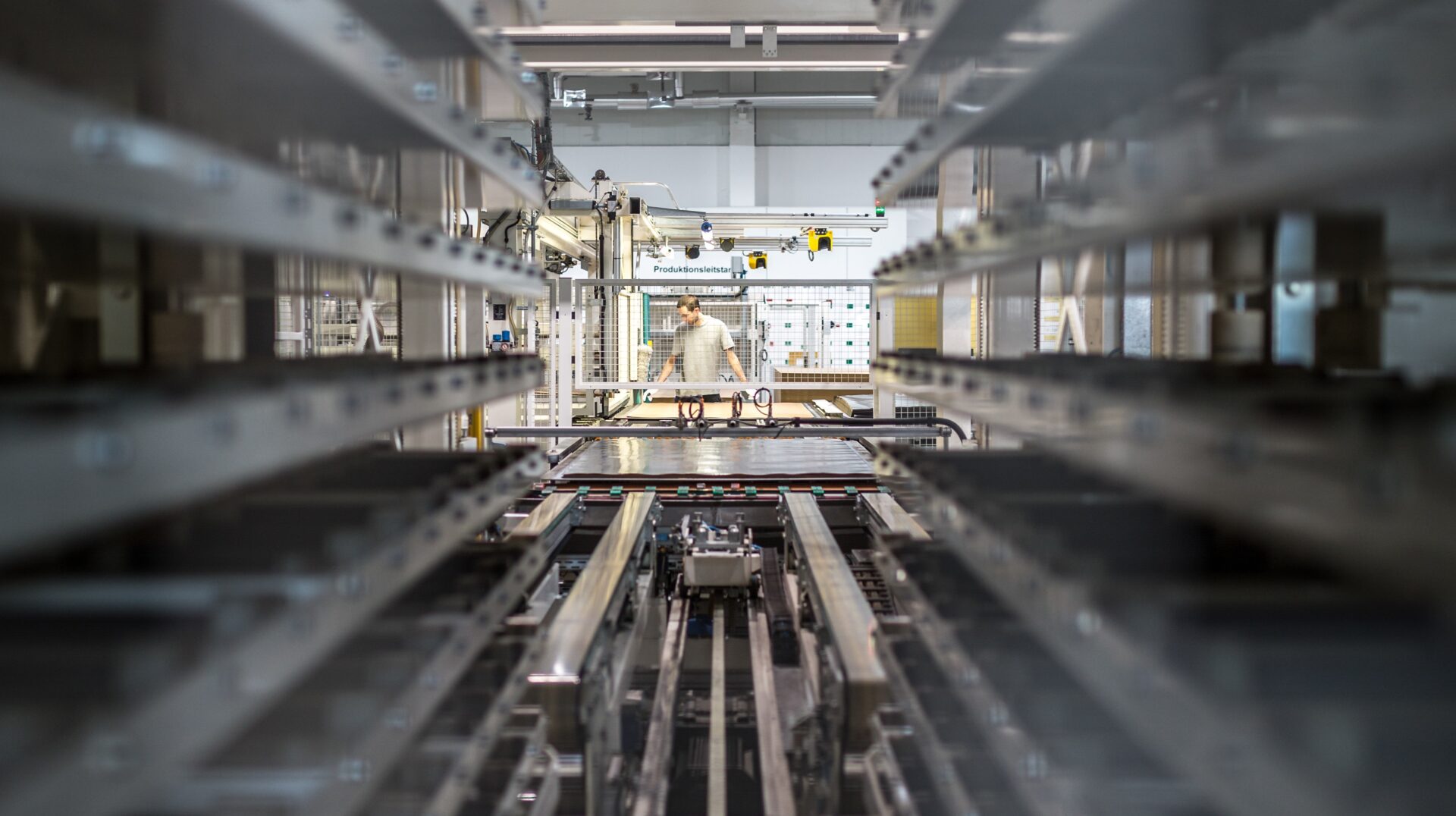 Eine Person arbeitet in einer hellen Fabrikumgebung, umgeben von Metallregalen mit Schienen im Vordergrund.