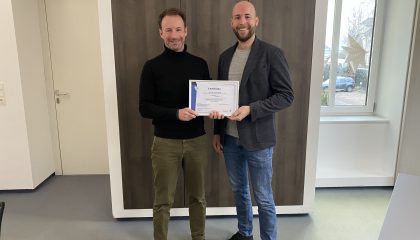 Zwei Männer stehend in einem Büro die gemeinsam eine Auszeichnung in Händen halten.